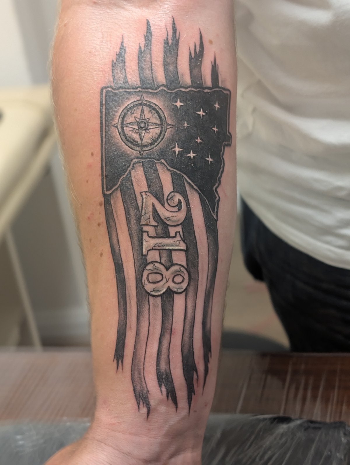 Black and grey 1988 compass and flag tattoo on the lower leg by Shawn Lowe at Fargo Tattoo in Fargo, North Dakota