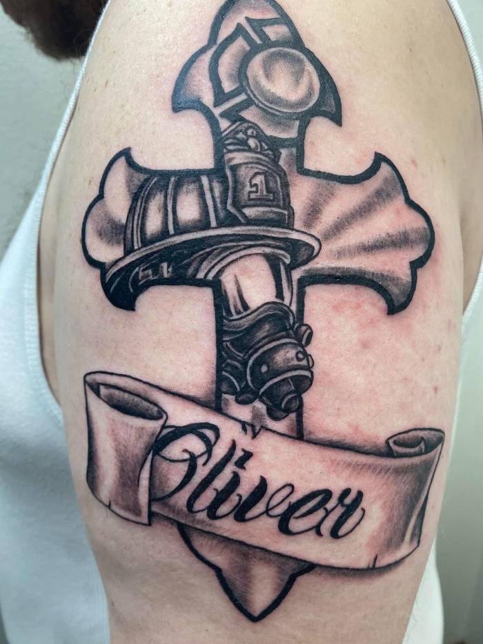 Firefighter memorial cross tattoo with helmet and Oliver name banner by Shawn Lowe at Fargo Tattoo in Fargo, North Dakota