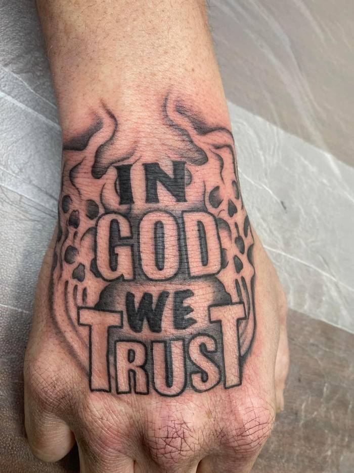 In God We Trust bold lettering hand tattoo with skull smoke detail by Shawn Lowe at Fargo Tattoo in Fargo, North Dakota