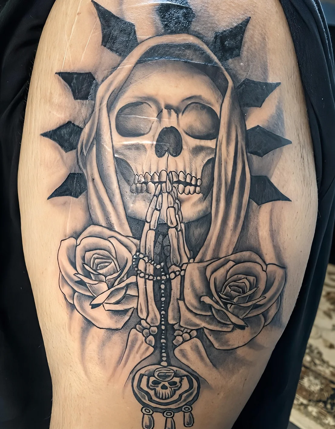 Black and grey tattoo of a skull, praying hands, roses, and rosary by Shawn Lowe at Fargo Tattoo in Fargo, North Dakota