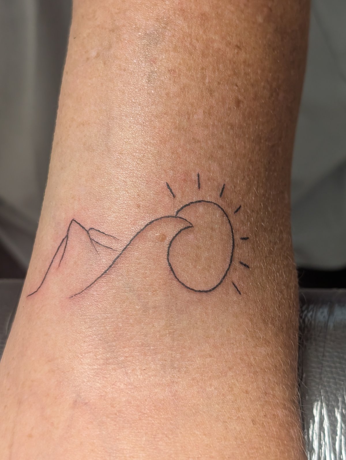 Fine line tattoo of mountains, sun, and moon on the forearm by Shawn Lowe at Fargo Tattoo in Fargo, North Dakota